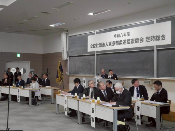 Panelists in a conference room seated at long desks with bottled drinks, a Japanese banner overhead.